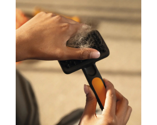 Mâini îndepărtând păr de animale de pe o perie pentru animale