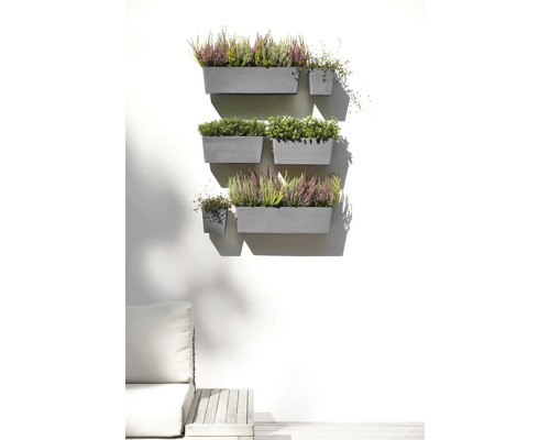 Ghivece de perete gri cu iarbă neagră și plante verzi, dispuse ca o grădină verticală organizată pe un perete de terasă luminos.