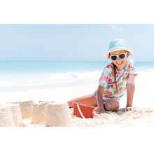 Fată cu ochelari de soare și pălărie construind castele de nisip pe plajă