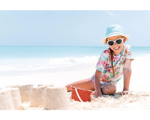 Fată cu ochelari de soare și pălărie construind castele de nisip pe plajă