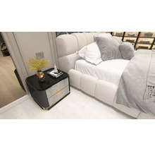 Dormitor modern cu o noptieră negru-gri cu detalii aurii lângă un pat tapițat alb.