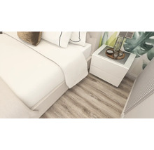 Dormitor luminos cu pardoseală cu aspect de stejar, pat dublu alb și noptieră albă asortată.