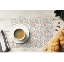 Suport pentru farfurie dreptunghiular cu model de flori mici roz și albastre, cu o ceașcă de cafea și produse de patiserie pe o masă din lemn deschis.