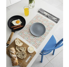 Suport de farfurie cu imprimeu floral pe o masă albă cu farfurie gri, tigaie cu ou ochi, pâine feliată pe un tocător și un pahar de suc.