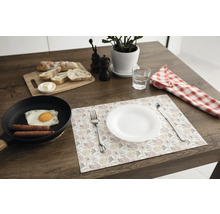 Suport pentru farfurii cu model floral pe o masă din lemn închis la culoare, cu farfurie albă, tacâmuri, tigaie cu mic dejun și tocător.