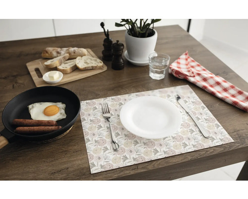 Suport pentru farfurii cu model floral pe o masă din lemn închis la culoare, cu farfurie albă, tacâmuri, tigaie cu mic dejun și tocător.