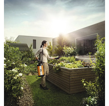 O femeie folosește un pulverizator de grădină într-un strat de flori ridicat în grădină.