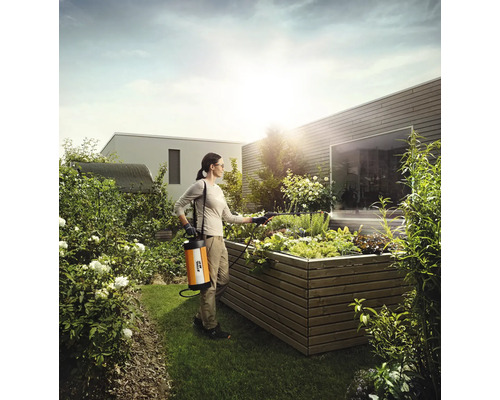 O femeie folosește un pulverizator de grădină într-un strat de flori ridicat în grădină.