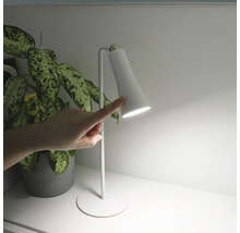 Lampă de birou albă operată cu un deget, lângă o plantă de interior.