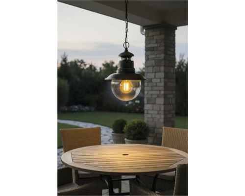 Lampa suspendată metalică cu glob de sticlă transparentă deasupra unei mese de grădină