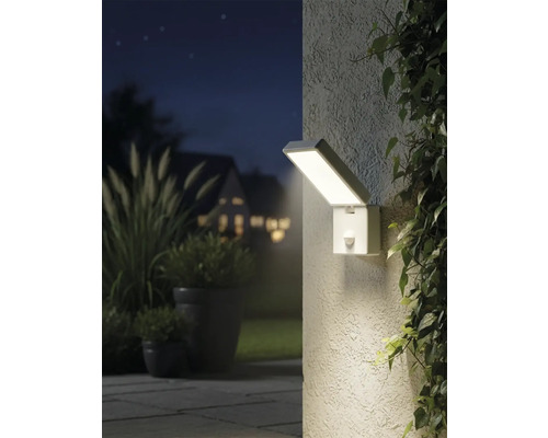 Imagine de exterior iluminată, cu o lampă de perete dreptunghiulară cu senzor de mișcare lângă plante.