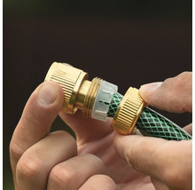 Mâini care montează un conector de furtun din alamă pe un furtun de grădină verde.