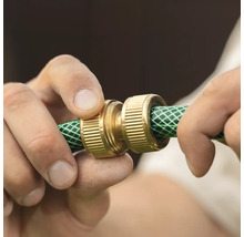 Mâini care instalează un conector de furtun din alamă pe un furtun de grădină verde.