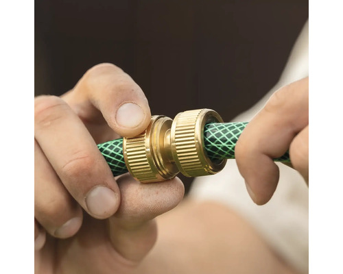 Mâini care instalează un conector de furtun din alamă pe un furtun de grădină verde.