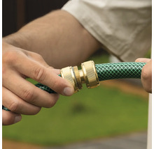 Mâini care conectează două cuplaje din alamă pe un furtun de grădină verde.
