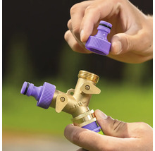 Mâini care montează un conector de furtun violet pe un distribuitor cu două căi din alamă pentru furtunul de grădină.