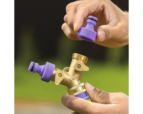 Mâini care montează un conector de furtun violet pe un distribuitor cu două căi din alamă pentru furtunul de grădină.