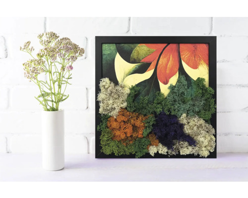Tablou din mușchi în ramă neagră cu mușchi colorat și imprimeu floral lângă o vază albă cu flori.