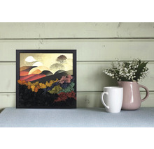 Tablou pătrat în ramă neagră cu peisaj stilizat din mușchi colorat, decorat lângă o cană albă și o vază roz pe o masă.