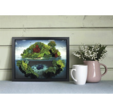 Ramă neagră cu tablou din mușchi, reprezentând o insulă cu reflexie, lângă o cană și un urcior cu flori în fața unui perete de lemn.