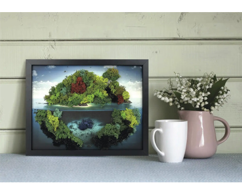 Ramă neagră cu tablou din mușchi, reprezentând o insulă cu reflexie, lângă o cană și un urcior cu flori în fața unui perete de lemn.