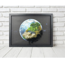 Tablou cu mușchi cu motiv glob pământesc în ramă neagră în fața unui perete de cărămidă.