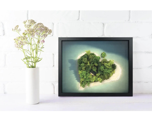 Decorațiune de perete cu un tablou din mușchi în formă de inimă în ramă neagră, lângă o vază cu flori în fața unui perete de cărămidă albă.