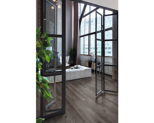 Zonă de zi modernă cu pardoseală închisă la culoare cu aspect de lemn, ferestre industriale mari și mobilier deschis la culoare.