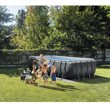 Piscină supraterană dreptunghiulară gri închis cu cadru metalic într-o grădină luminoasă. O familie stă lângă ea pe iarbă.