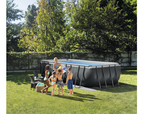 Piscină supraterană dreptunghiulară gri închis cu cadru metalic într-o grădină luminoasă. O familie stă lângă ea pe iarbă.