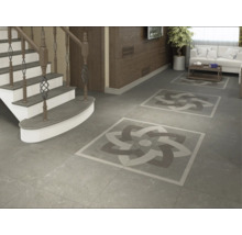 Interior spațios cu plăci de gresie gri cu modele florale geometrice mari lângă o scară și o zonă de zi luminoasă cu canapea.