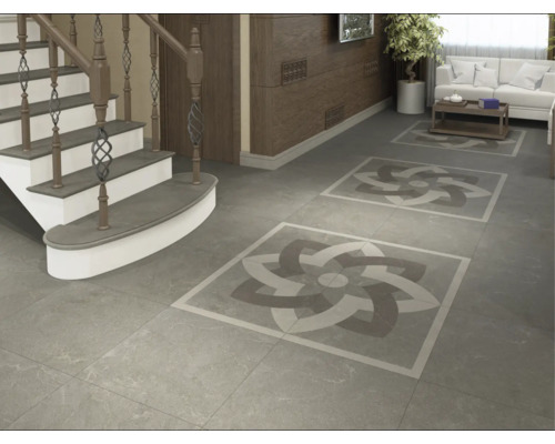 Interior spațios cu plăci de gresie gri cu modele florale geometrice mari lângă o scară și o zonă de zi luminoasă cu canapea.