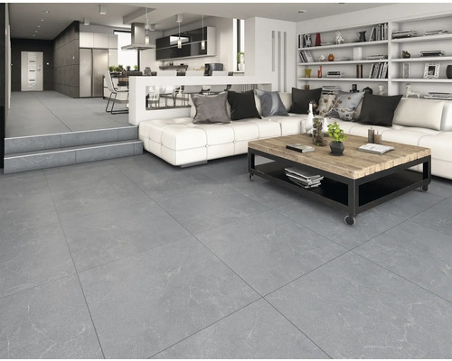 Gresie gri de format mare cu aspect de piatră într-un living modern și luminos, cu canapea albă și bucătărie deschisă.