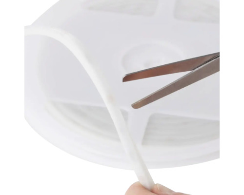 Bandă LED albă flexibilă scurtată cu o foarfecă metalică pe o rolă de plastic.