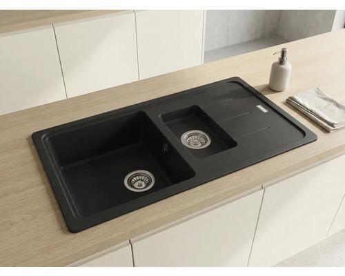 Chiuvetă încastrată cu o cuvă și jumătate și picurător din material compozit într-un blat de lemn deschis și bucătărie albă.