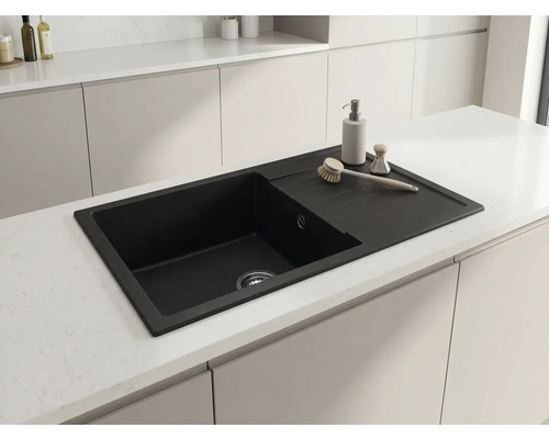 Chiuvetă de bucătărie neagră cu picurător montată într-o insulă de bucătărie modernă și deschisă la culoare.