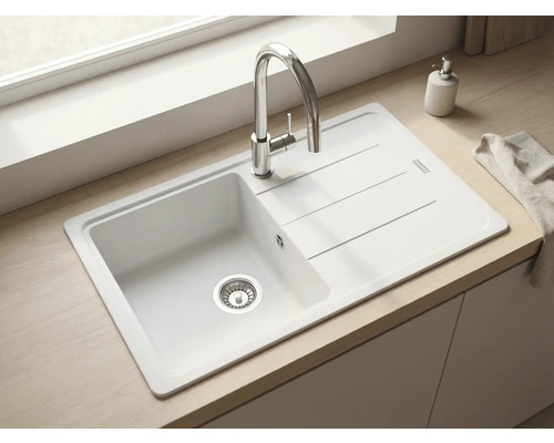 Bucătărie luminoasă și modernă cu o chiuvetă încorporabilă albă, picurător și baterie cromată pe un blat cu aspect de lemn.