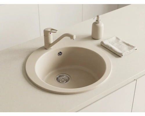 Chiuvetă de bucătărie rotundă din material compozit cu baterie monocomandă asortată, dozator de săpun și lavetă pe un blat de lucru deschis.