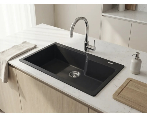 Chiuveta neagra moderna din compozit in blat alb cu aspect de marmura pe o insula de bucatarie luminoasa cu baterie cromata curbata.