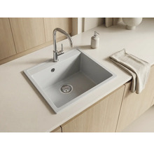 Bucătărie luminoasă și organizată cu chiuvetă încorporată modernă din compozit, baterie cromată, blat alb și dulapuri din lemn.