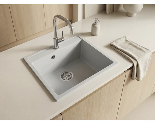 Bucătărie luminoasă și organizată cu chiuvetă încorporată modernă din compozit, baterie cromată, blat alb și dulapuri din lemn.