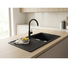 Chiuvetă de bucătărie încorporată, neagră, cu picurător și baterie neagră înaltă, pe o insulă de bucătărie cu blat din lemn deschis.