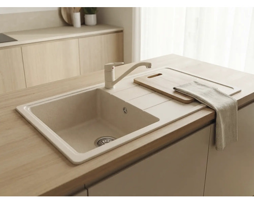 Chiuvetă încorporabilă bej cu baterie asortată într-o bucătărie din lemn deschis. Include picurător, tocător și prosop de bucătărie.