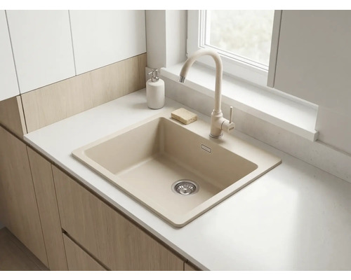 Chiuvetă de bucătărie bej cu baterie asortată pe un blat alb și dulapuri din lemn deschis într-o bucătărie luminoasă.