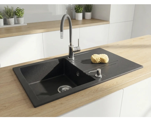 Chiuvetă de bucătărie încastrată din granit negru, cu picurător, baterie înaltă și dozator de săpun pe un blat din lemn deschis la culoare.