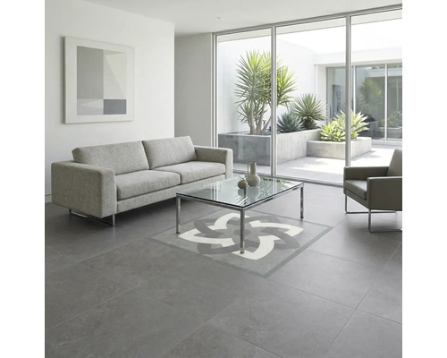 Living modern cu gresie gri, model decorativ central, canapea gri și masă de sticlă în fața unui perete de sticlă spre zona exterioară.