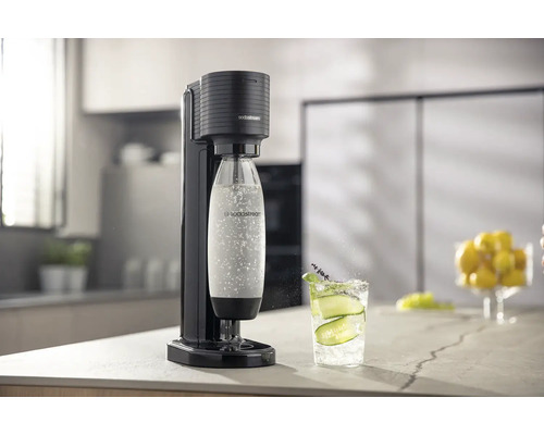 Aparat pentru apă minerală SodaStream Terra negru într-o bucătărie luminoasă și organizată, cu o sticlă de carbonatare și un pahar cu apă.
