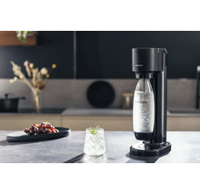 Aparat de făcut sifon SodaStream Terra negru într-o bucătărie modernă și luminoasă cu o sticlă de apă acidulată și un pahar cu gheață.