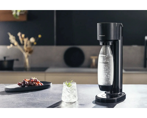 Aparat de făcut sifon SodaStream Terra negru într-o bucătărie modernă și luminoasă cu o sticlă de apă acidulată și un pahar cu gheață.