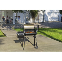 Grătar smoker negru cu capac deschis și carne pe grătar, amplasat pe o terasă din lemn în fața unei case albe.